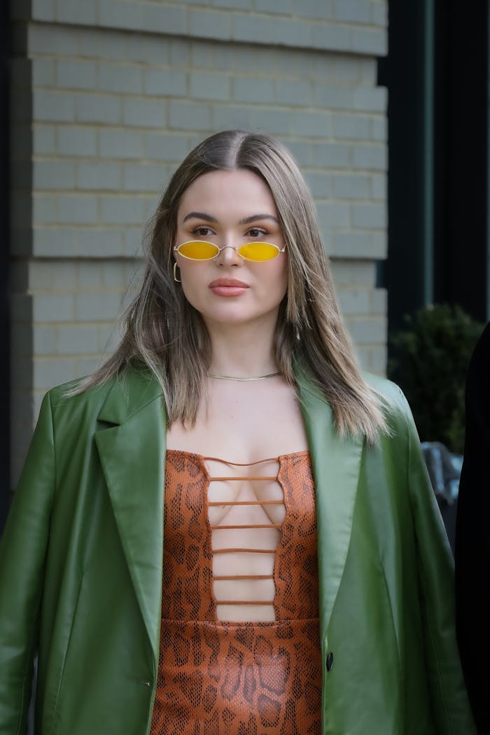Stylish woman wearing a green jacket, animal print dress, and yellow sunglasses outdoors.