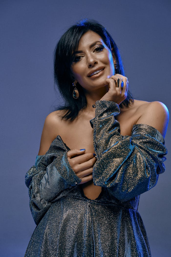 A glamorous woman posing confidently in a shimmering gown with blue lighting accents.